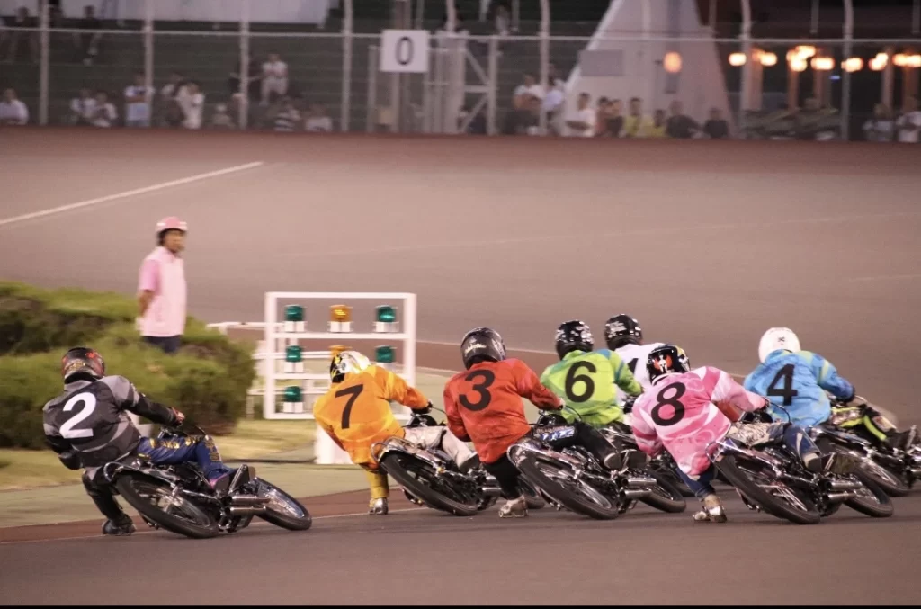 Auto Race riders accelerating from the starting line in Japan, showing colorful racing suits and the unique handicap start system.