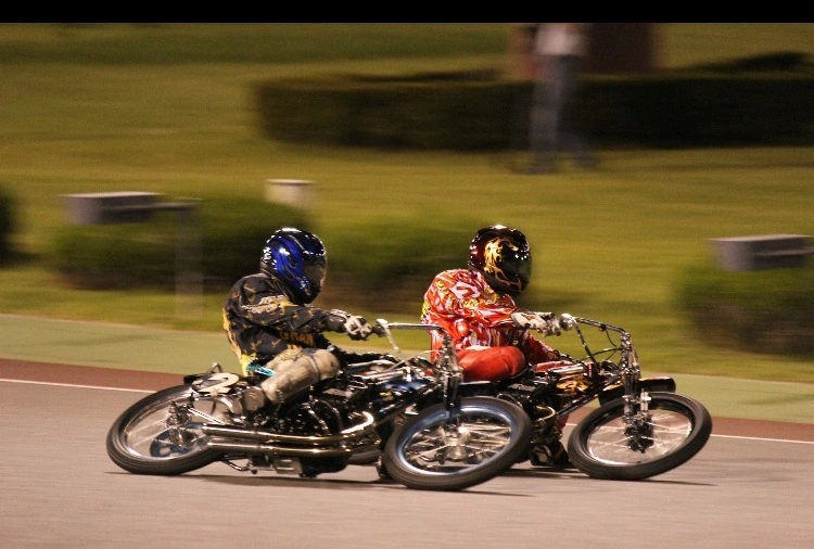 Two Auto Race riders competing at high speed on an oval track in Japan, showcasing the thrilling no-brake racing style.