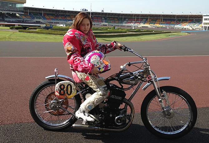 Female Auto Race rider sitting on an official AR600 machine at Kawaguchi Auto Race track in Japan, representing the new generation of racers.